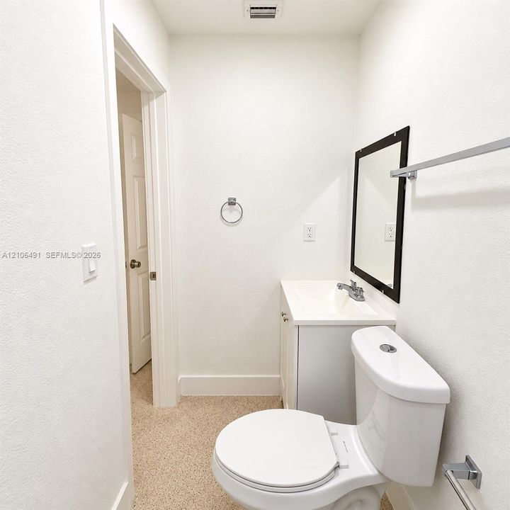 Bathroom featuring a white vanity cabinet with a integrated sink, polished metal hardware, a wall-mounted mirror with a dark frame, and a chrome towel bar