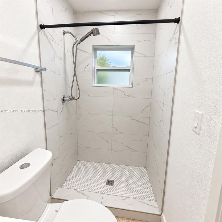Walk-in shower featuring large-format stone-pattern wall tile, circular mosaic floor tile, hand-held shower fixture, and a built-in window