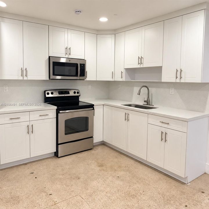 Kitchen featuring white shaker-style cabinetry, stainless steel appliances, solid surface countertops, and an undermount sink with a gooseneck faucet