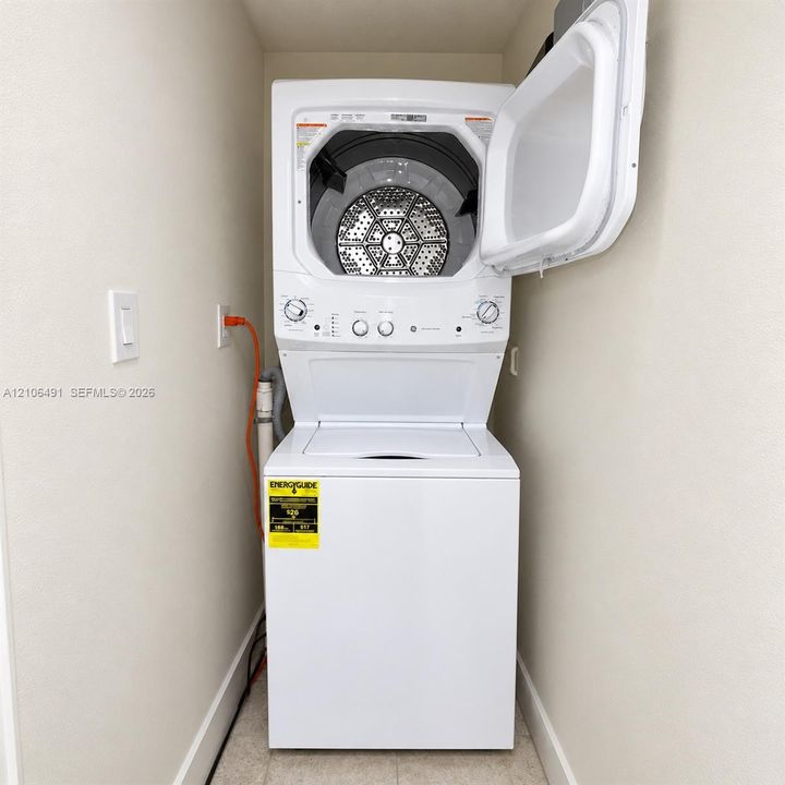 White stacked laundry unit featuring a top-loading washer and front-loading dryer with a metallic drum finish