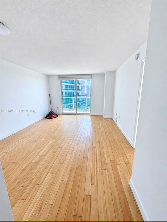 Open interior space featuring wood-finish flooring, neutral wall tones, and floor-to-ceiling sliding glass doors opening to a balcony
