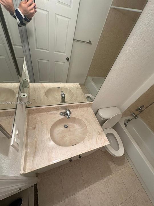 Bathroom featuring a vanity with an integrated basin, a large wall-mounted mirror, ceramic tile flooring, and a shower-tub combination with a tiled surround