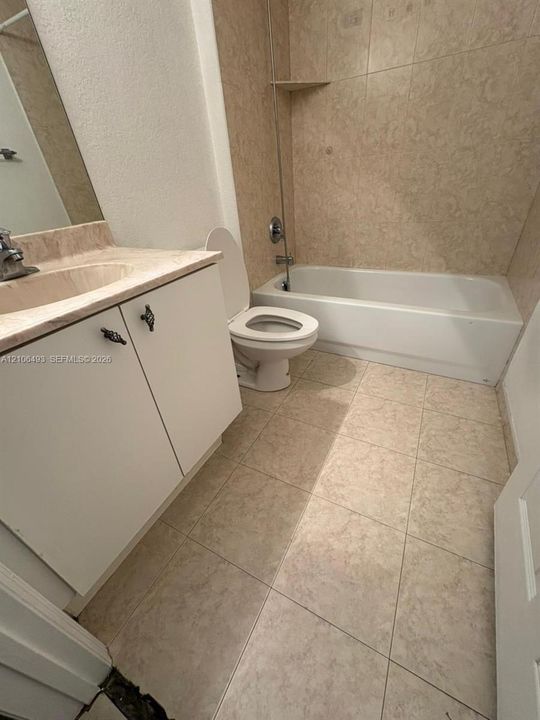 Bathroom featuring tile flooring, a vanity with a stone-top surface, an integrated sink basin, and a tub-shower combination with tiled surround