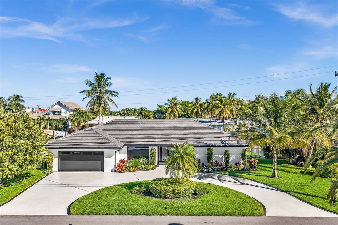Single-story residence featuring a low-pitched tiled roof, a circular concrete driveway, and an attached two-car garage, complemented by mature tropical landscaping