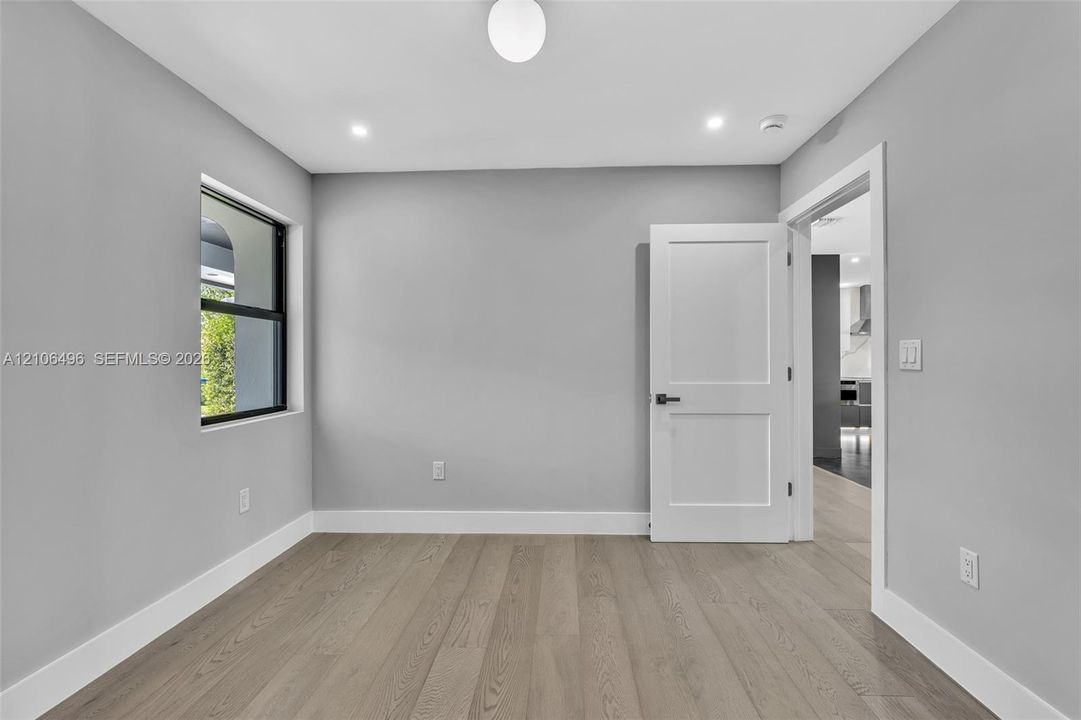 Neutral-toned interior room featuring wood-finish flooring, recessed lighting, a globe flush-mount fixture, a window with a black frame, and a solid-core two-panel interior door