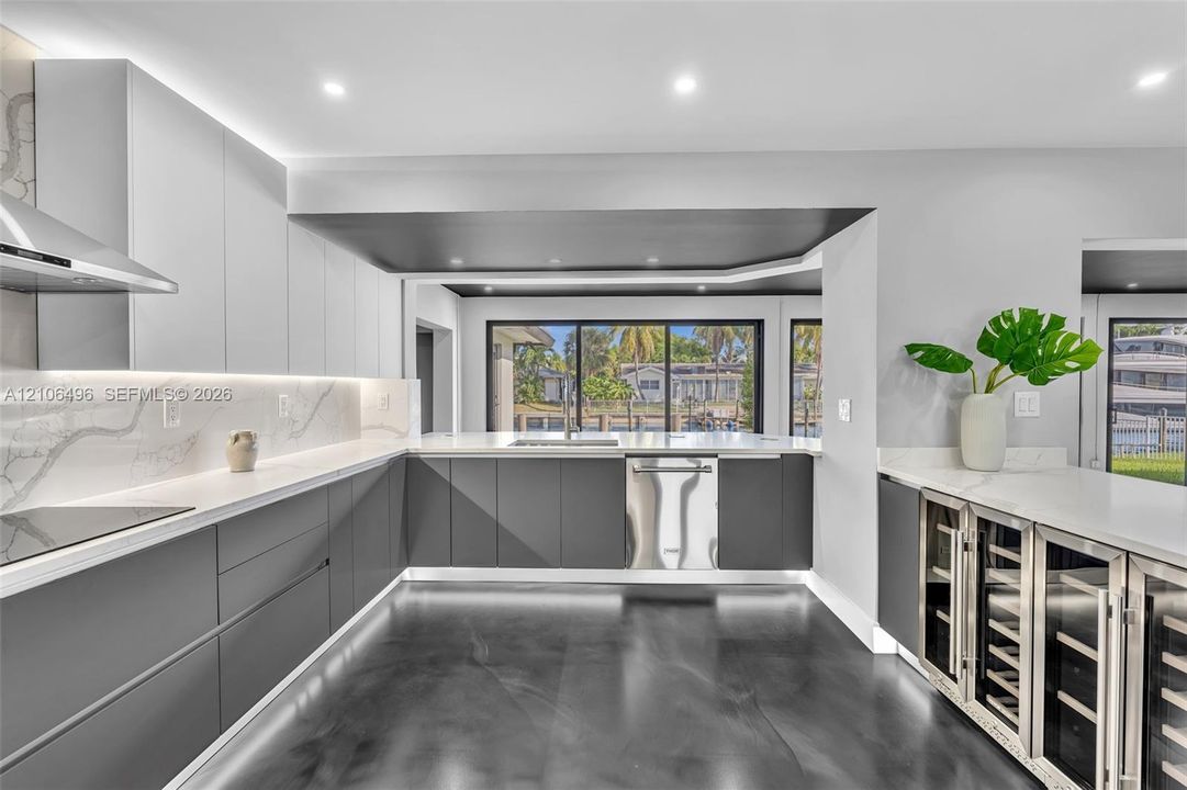 Kitchen featuring flat-panel cabinetry, light-toned stone-finish backsplash, built-in stainless steel appliances, polished flooring, and dual glass-door beverage refrigerators
