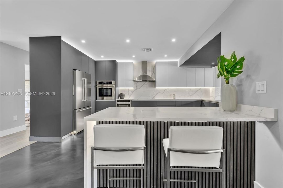 Modern kitchen featuring dual-tone cabinetry, quartz countertops, stainless steel appliances, an island with slatted detailing, and under-cabinet lighting