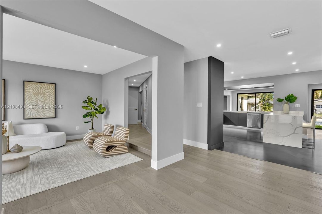 Open-concept floor plan featuring wood-finish flooring, recessed lighting, a stone-surfaced kitchen island, and a dark-toned accent pillar