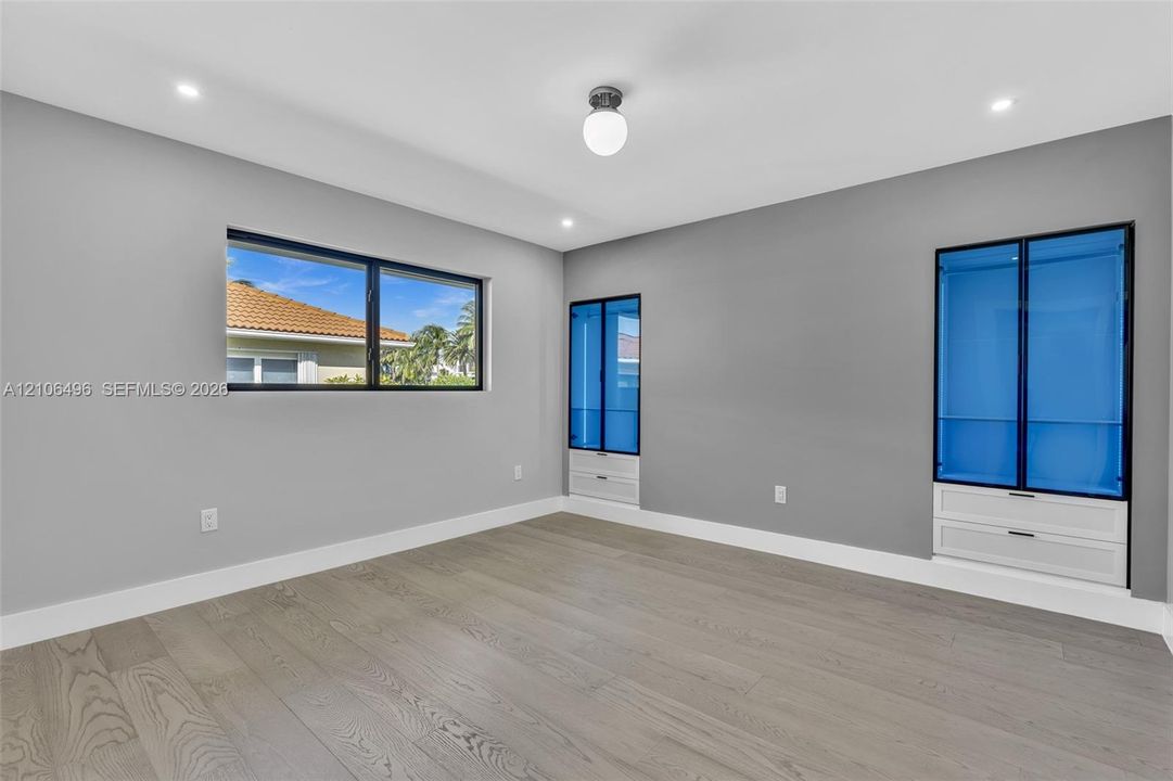 Room featuring wood-finish flooring, recessed lighting, horizontal window with black trim, and dual built-in floor-to-ceiling cabinets with glass doors and integrated drawers