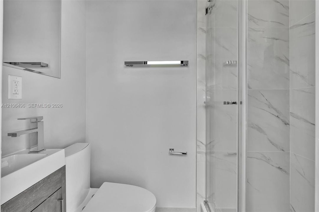 Modern bathroom featuring a wood-finish vanity, rectangular vessel sink with a polished chrome faucet, glass-enclosed shower with tiled walls, and polished chrome hardware