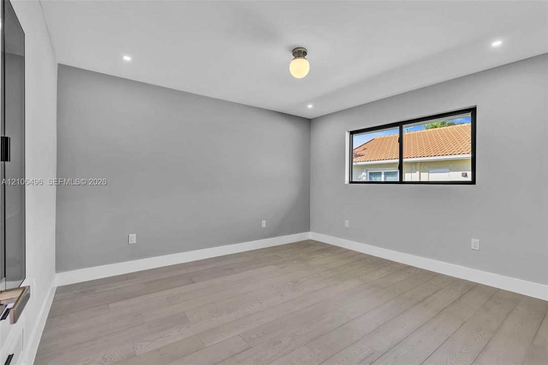 Neutral-toned interior room featuring wood-finish flooring, recessed lighting, a globe-style overhead light fixture, and a black-framed window