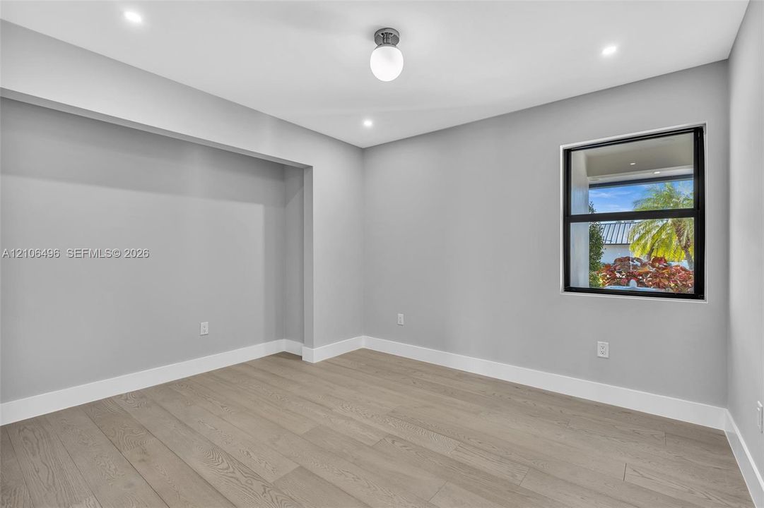 Neutral-toned room featuring wood-finish flooring, recessed lighting, a modern globe-style ceiling fixture, and a built-in recessed wall alcove