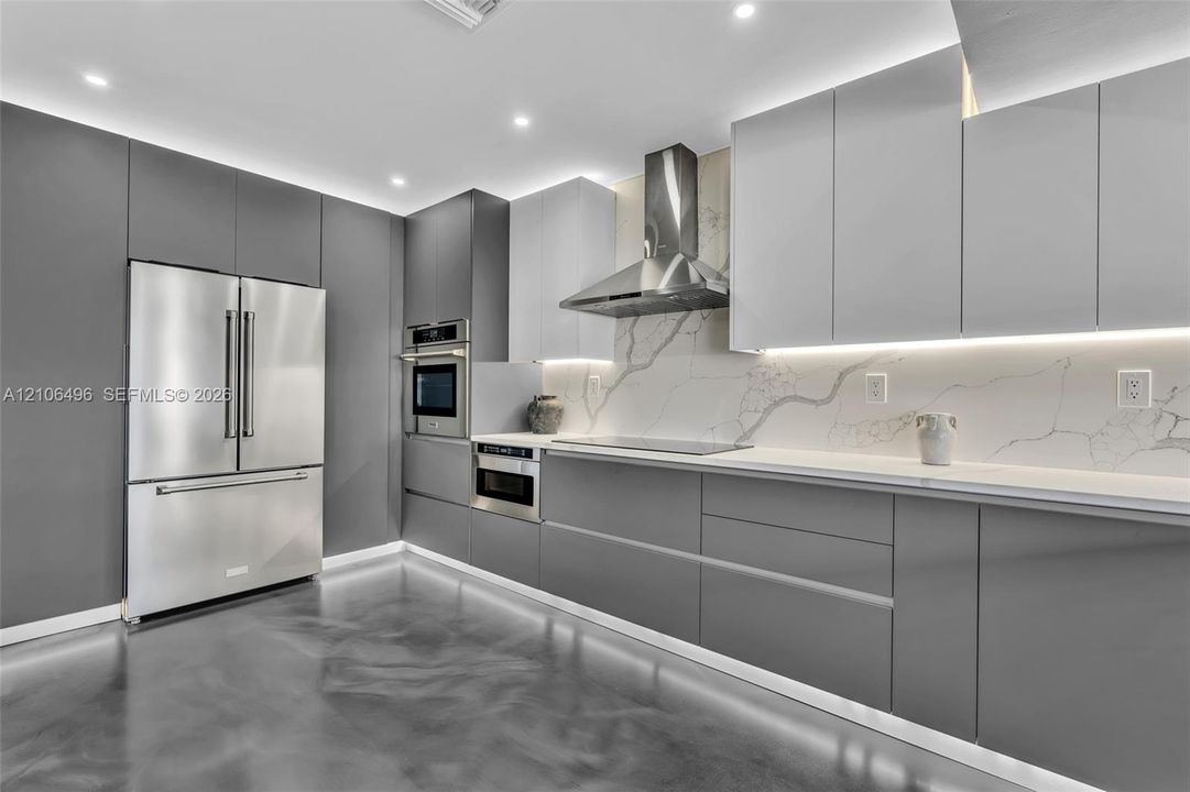 Kitchen featuring floor-to-ceiling cabinetry, stainless steel appliances, stone-surface backsplash, integrated under-cabinet lighting, and polished concrete flooring