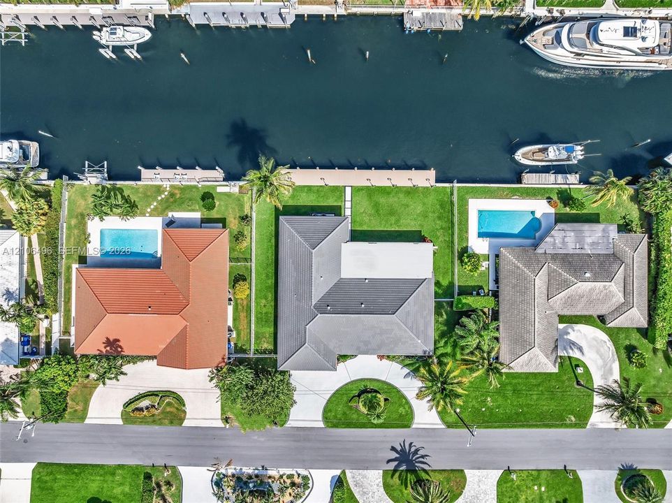 Waterfront property featuring a private boat dock, rectangular swimming pool, manicured lawn, and multi-faceted hipped roofline