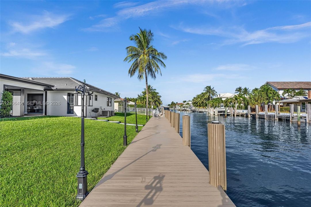 Waterfront property featuring a private composite dock, manicured lawn, exterior decorative post lighting, and direct canal access
