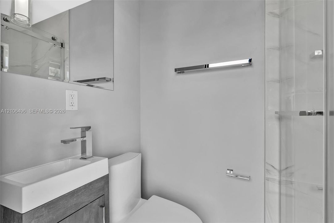 Modern bathroom featuring a wood-finish vanity, white rectangular vessel sink, polished chrome fixtures, wall-mounted mirror, and walk-in shower with stone-patterned tile
