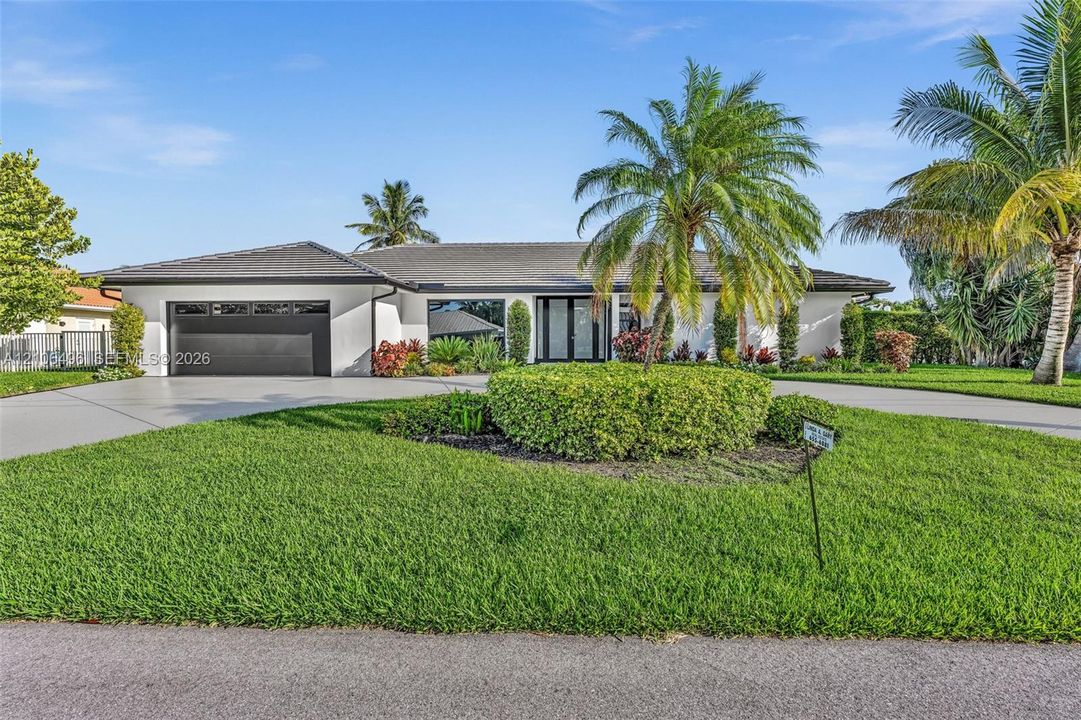 Single-story residence featuring a smooth stucco facade, hip roof with dark tiles, attached two-car garage, and manicured landscaping with established palm trees