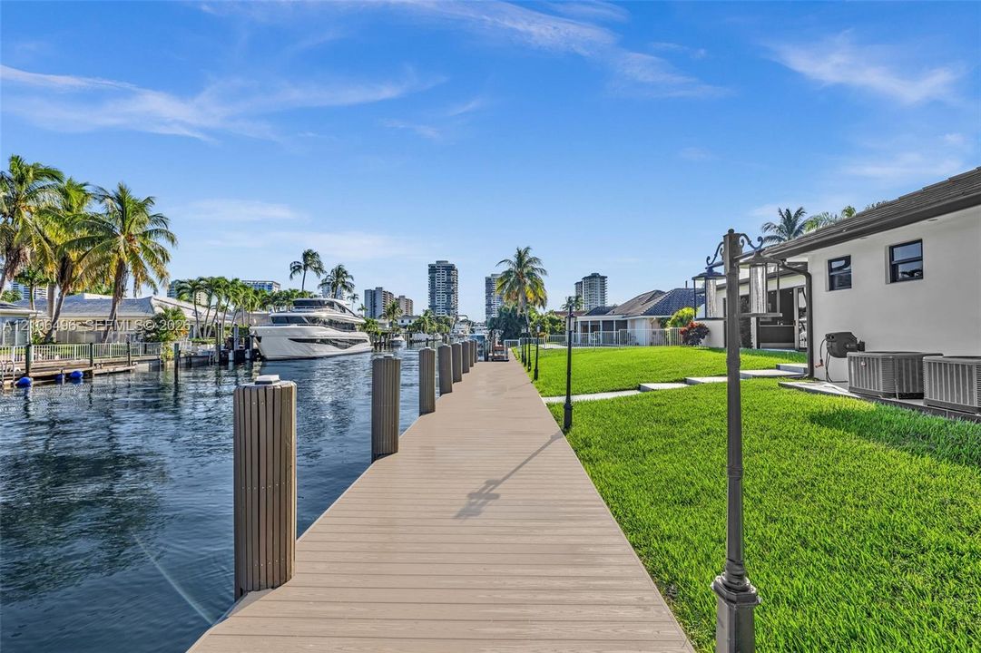 Waterfront property featuring a private bulkhead dock, manicured lawn, stone paver pathway, and nautical piling hardware