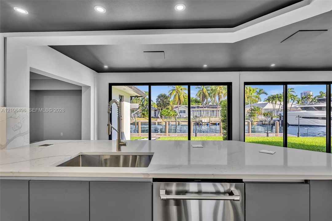 Kitchen featuring a stone-surface island, undermount stainless steel sink with a high-arc faucet, integrated stainless steel dishwasher, flat-panel cabinetry, and floor-to-ceiling glass sliding doors