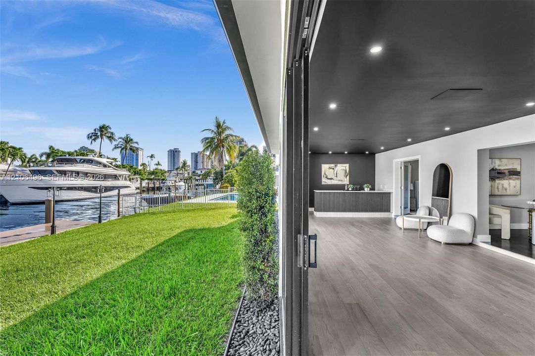 Waterfront property featuring a private boat dock, retractable glass wall system, recessed lighting, wood-finish flooring, and a built-in wet bar