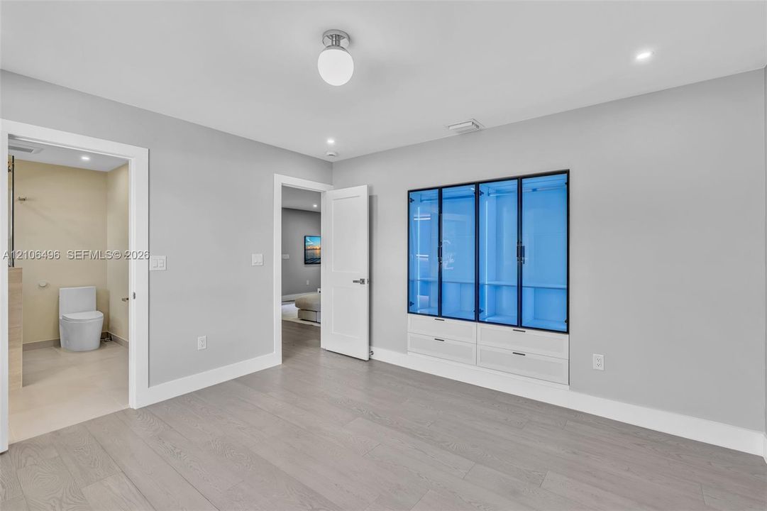 Built-in wall cabinetry with glass-panel doors and lower drawers, wood-finish flooring, and minimalist ceiling-mounted light fixture