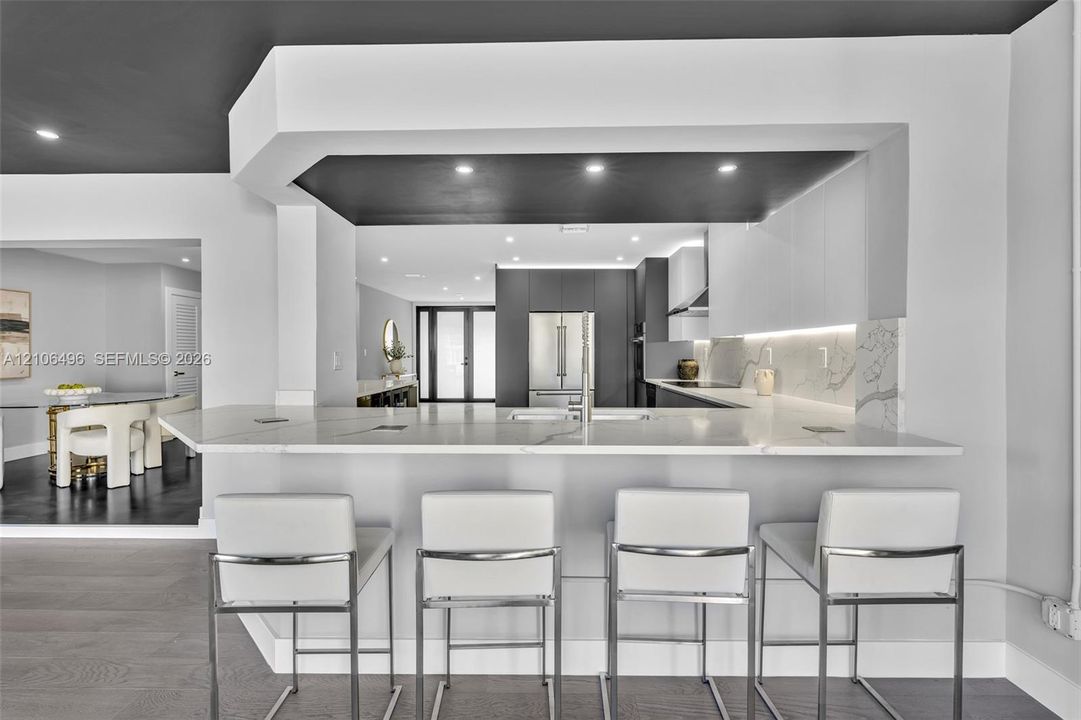 Kitchen featuring a peninsula with a stone-surfaced countertop, integrated under-cabinet lighting, full-height stone backsplash, flat-panel cabinetry, and recessed ceiling lighting