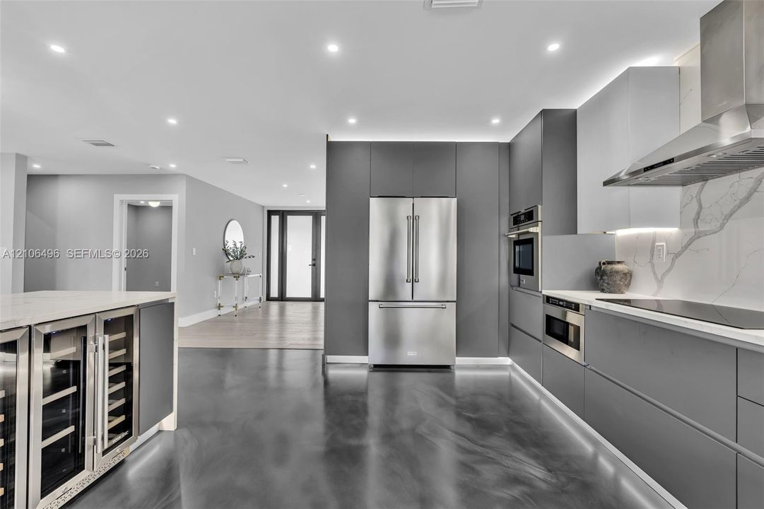 Modern kitchen featuring handleless cabinetry, stainless steel appliances, a built-in wine refrigerator, under-cabinet lighting, and a stone-patterned backsplash
