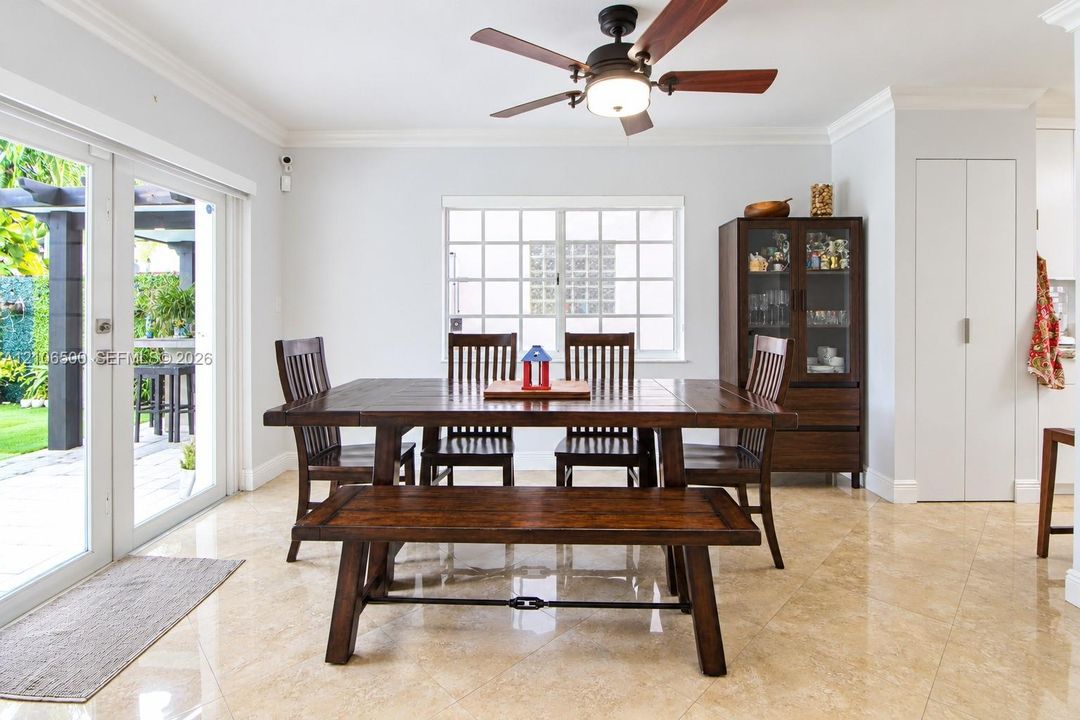 Polished stone tile flooring, crown molding, double French doors, large multi-pane window, and a central ceiling fan with integrated lighting