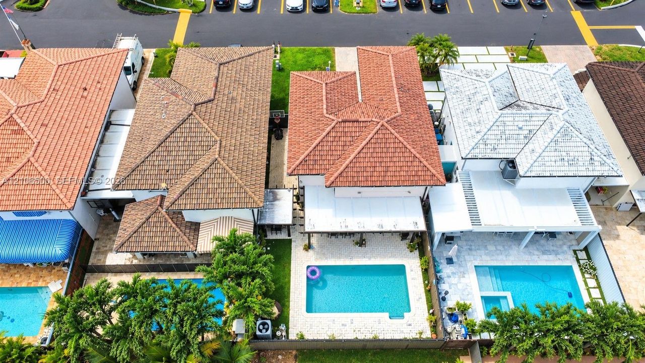Aerial view of a multi-story residence featuring a terracotta-tiled roof, an integrated swimming pool, and a paved hardscaped patio area