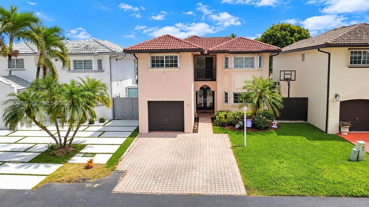 Two-story stucco exterior featuring a tile roof, paved driveway, single-car garage, and a covered entryway with a balcony