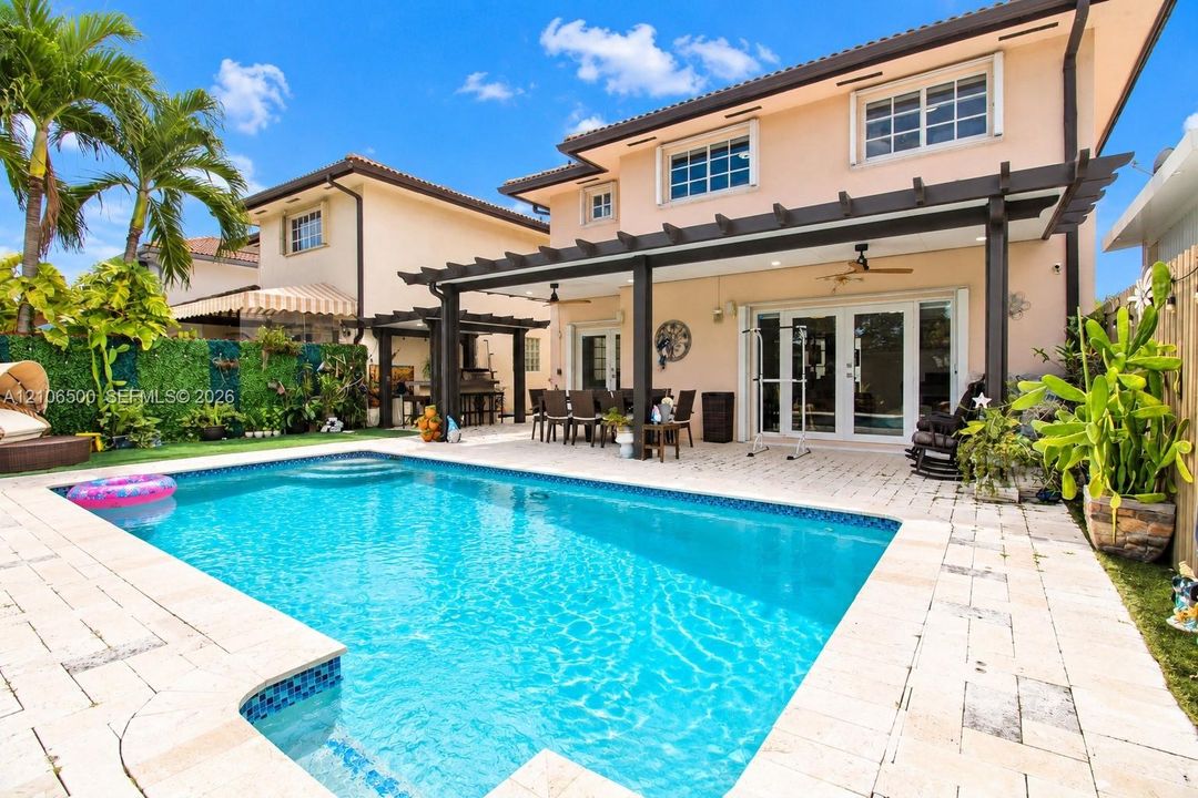 Backyard featuring an in-ground swimming pool, stone-paver decking, and a covered patio with a wooden pergola