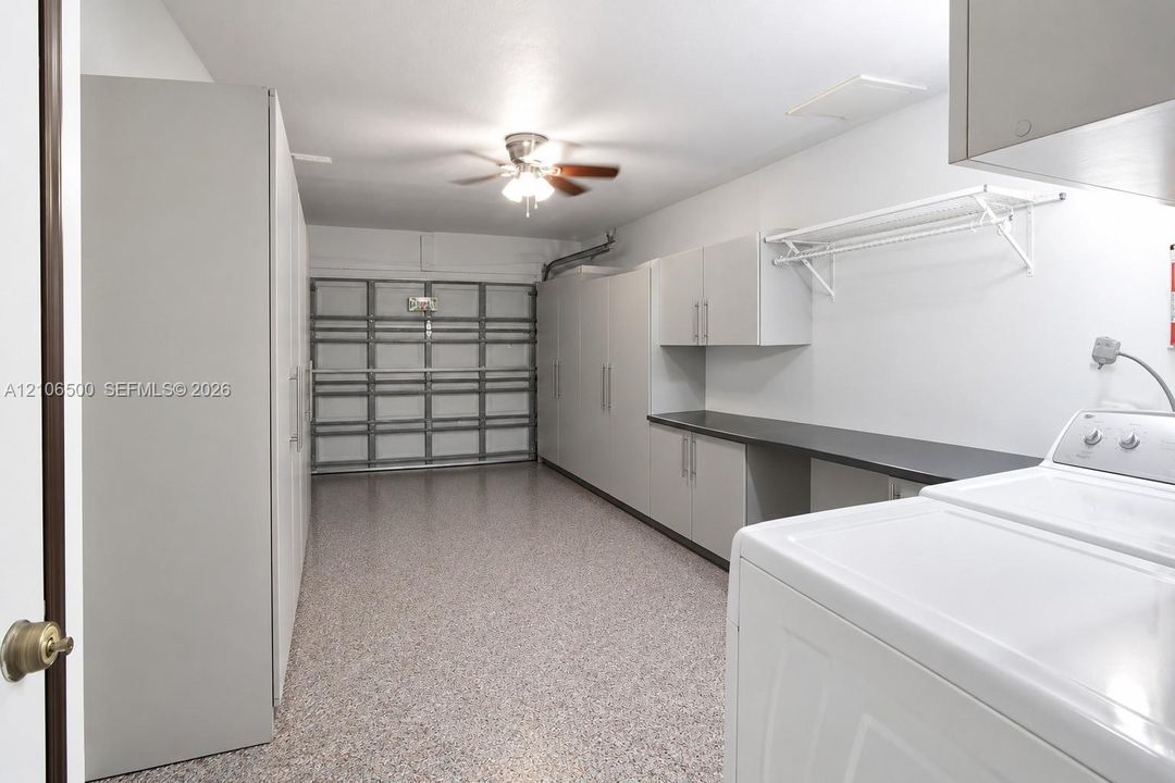 Attached garage featuring speckled epoxy flooring, built-in cabinetry with solid countertops, integrated wire shelving, and a ceiling fan with integrated lighting