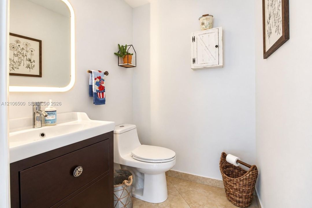Dark-finish wood vanity with integrated basin, polished chrome faucet, and rounded-corner LED-backlit mirror featuring neutral tile flooring and wall-mounted storage cabinetry