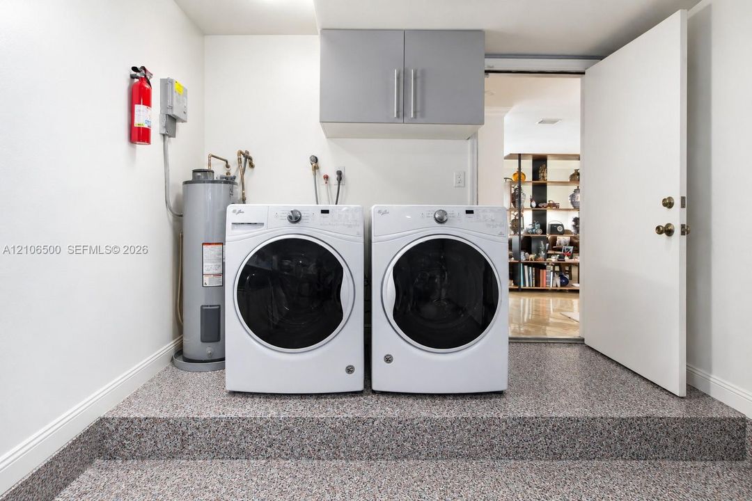 Laundry area featuring elevated speckled epoxy flooring, grey wall-mounted cabinetry, and dedicated hookups