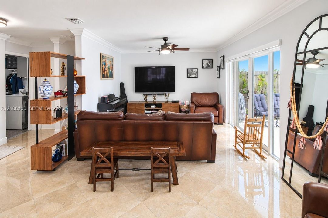 Living area featuring polished stone tile flooring, crown molding, a central ceiling fan, and sliding glass doors