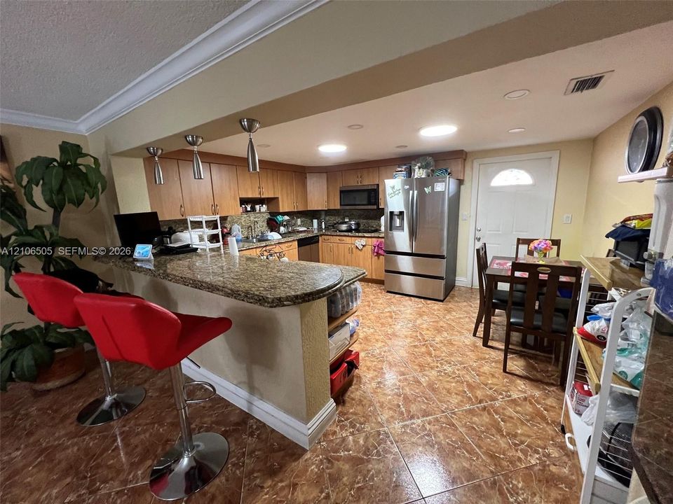 Kitchen featuring wood cabinetry, stone-finish countertops, stainless steel refrigerator, built-in microwave, and tile flooring