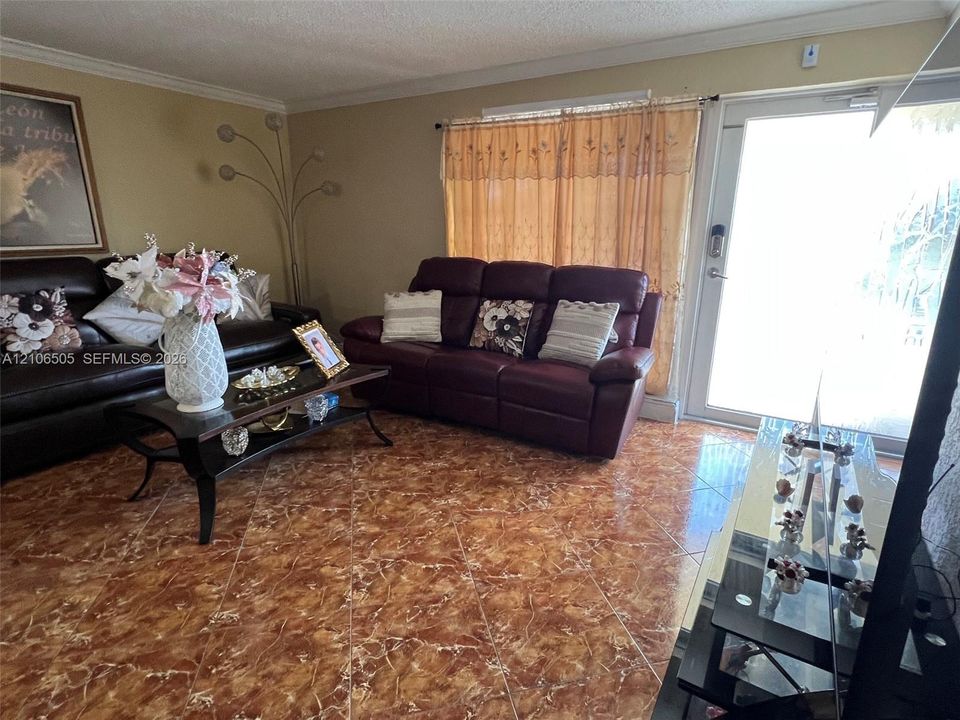 Living area featuring diagonal-set tile flooring, full-length glass-panel door, and crown molding