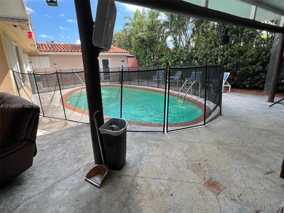 Covered outdoor patio with stamped concrete flooring, oval-shaped swimming pool, and terra-cotta tile roofline