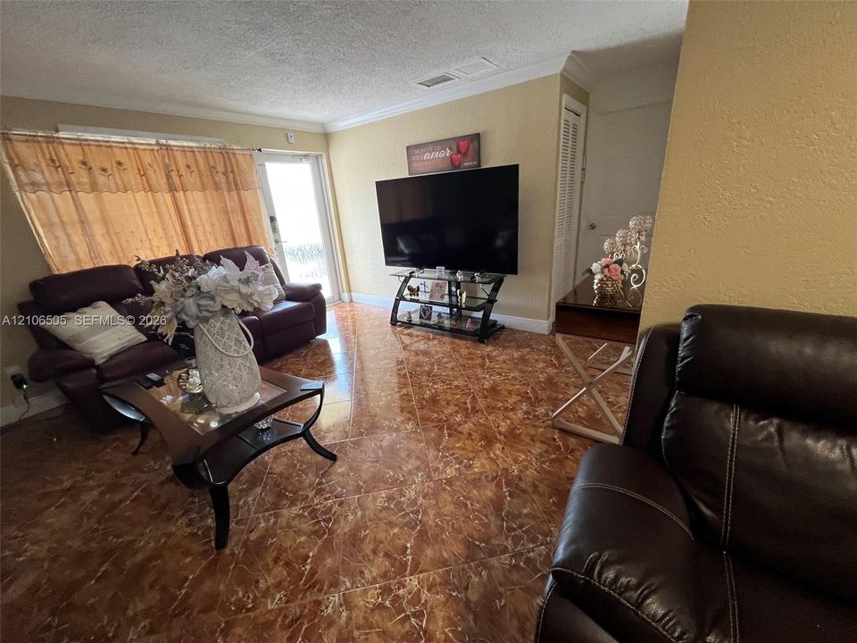 Living area featuring high-gloss tile flooring, crown molding, and a full-height glass door
