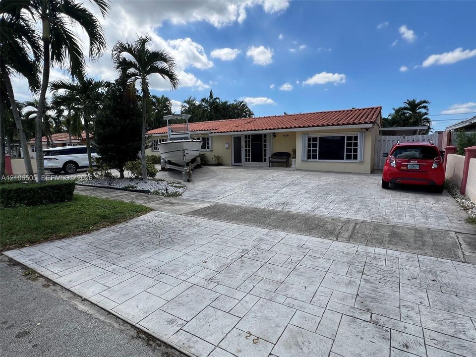 Single-story residence featuring a terracotta-tile roof, expansive stamped concrete driveway, and mature palm landscaping