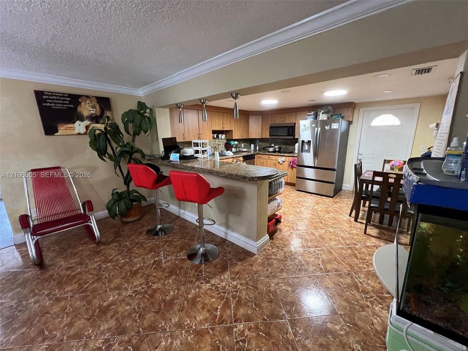 Kitchen featuring stone-finish countertops, stainless steel refrigerator, built-in microwave, wood-finish cabinetry, and ceramic tile flooring
