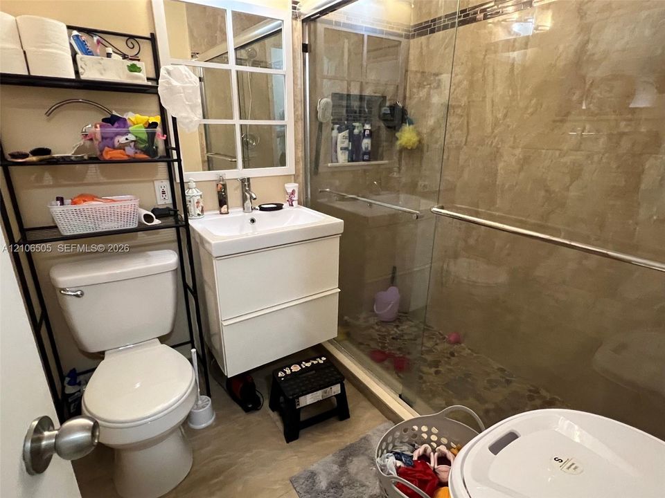 Wall-mounted white vanity with rectangular basin, glass-enclosed shower with tiled walls, and pebble-textured shower flooring