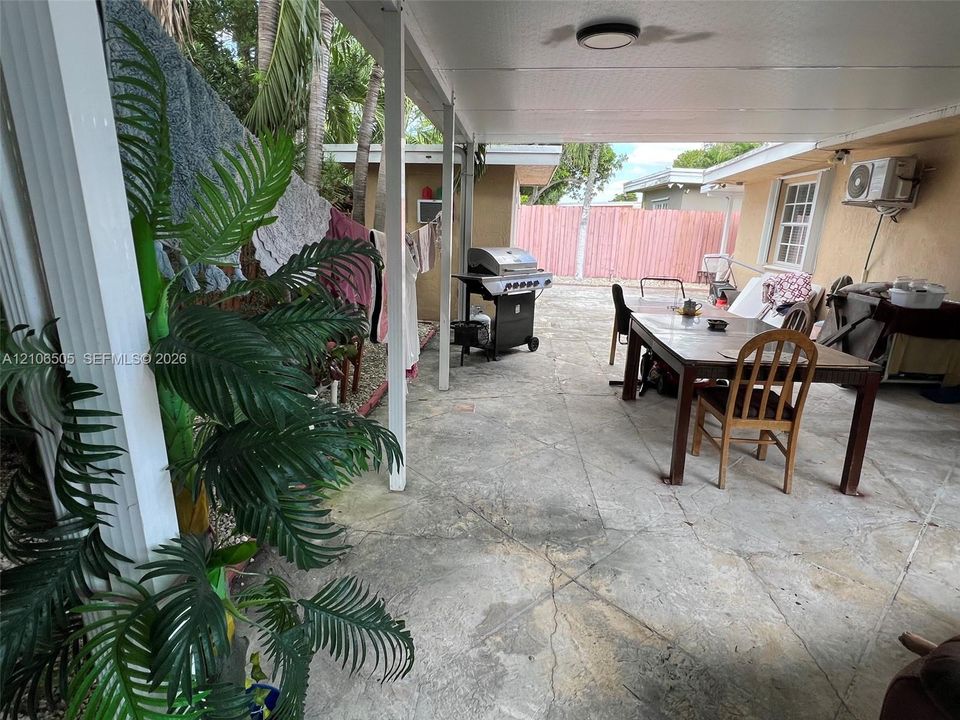 Covered concrete patio featuring white support columns, flush-mount lighting, and privacy fencing