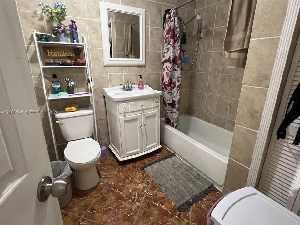 Bathroom featuring full-height wall tiling, white vanity cabinet with a integrated sink, framed wall mirror, and a tub-shower combination with handheld showerhead