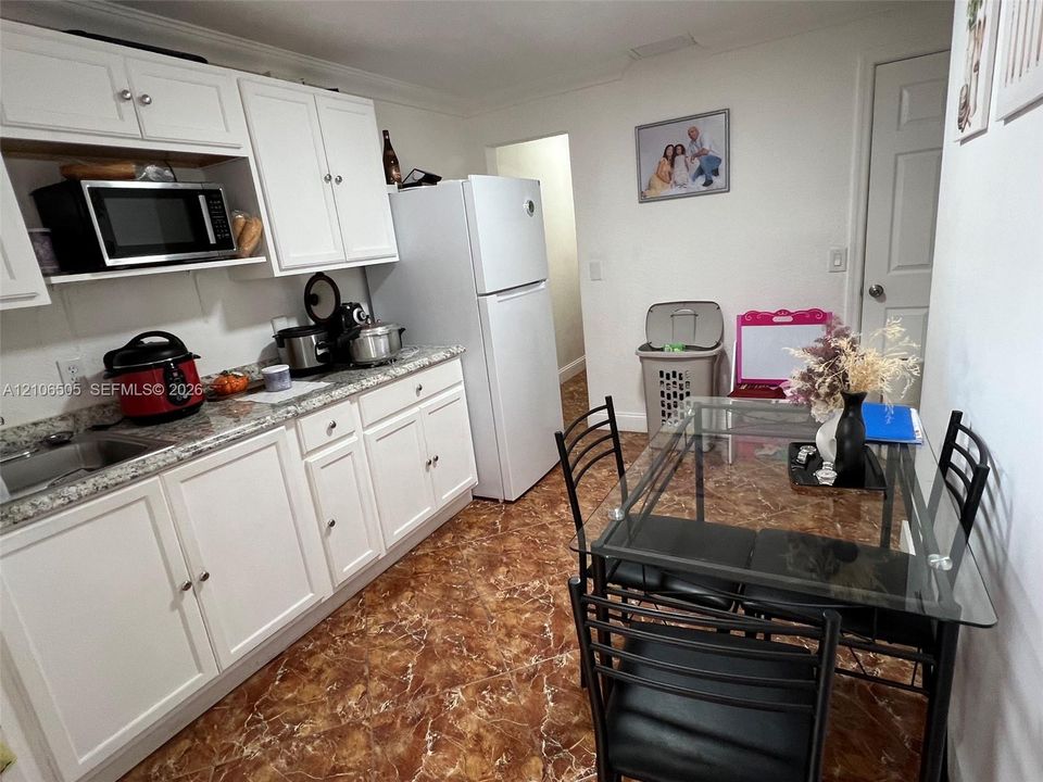 Kitchen featuring white shaker-style cabinetry, speckled stone-finish countertops, stainless steel sink, and polished tile flooring