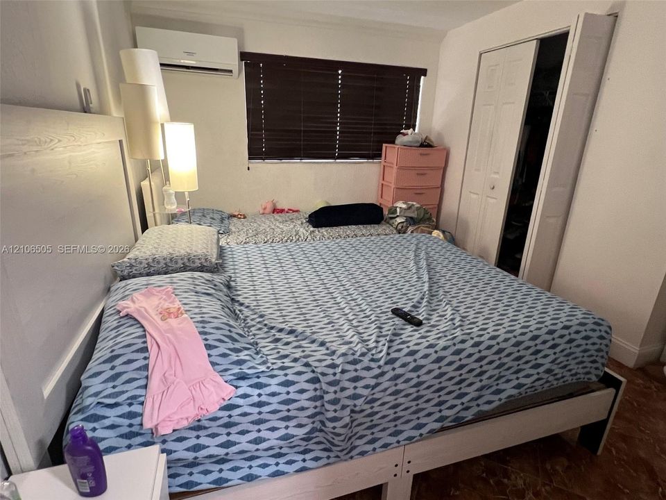 Wall-mounted ductless air conditioning unit, window with horizontal blinds, and a bi-fold closet door