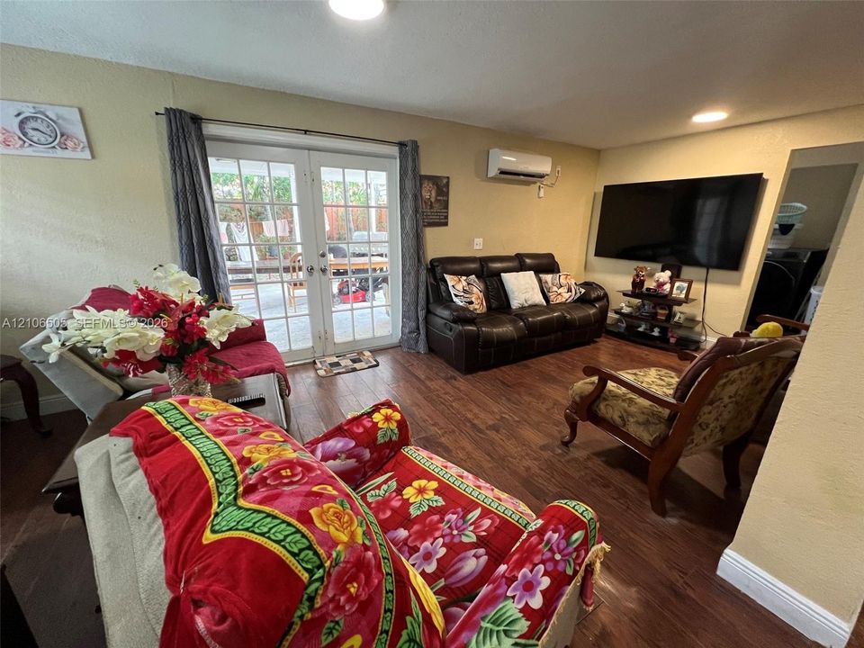 Living area featuring wood-finish flooring, white-framed French doors, and a wall-mounted ductless air conditioning unit