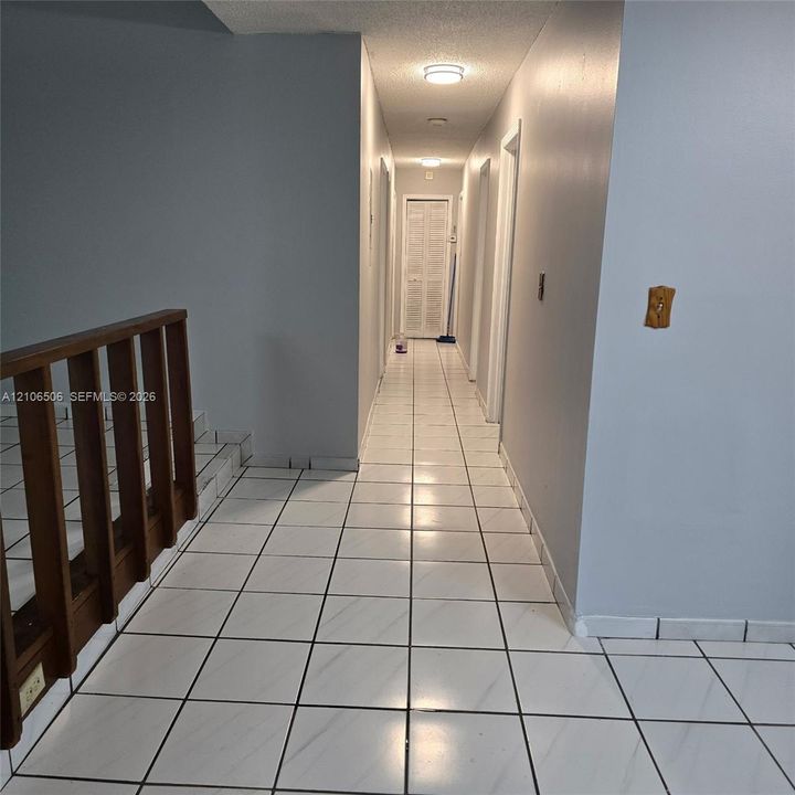 Hallway featuring ceramic tile flooring, a wood-finish staircase railing, and louvered closet doors