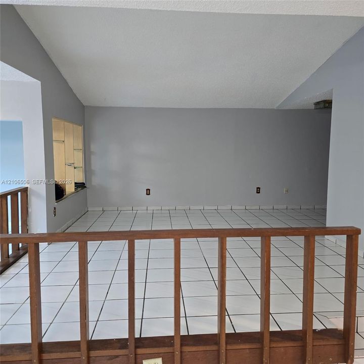 Vaulted ceilings featuring white tile flooring, built-in shelving, and a wood-slat railing