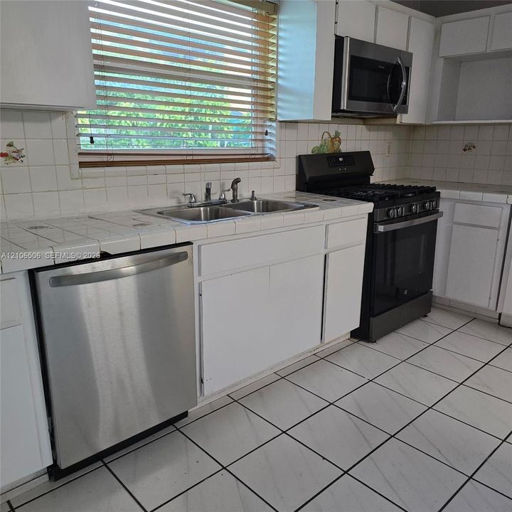 Kitchen featuring white cabinetry, stainless steel dishwasher, integrated microwave, dual-basin stainless steel sink, and ceramic tile countertops
